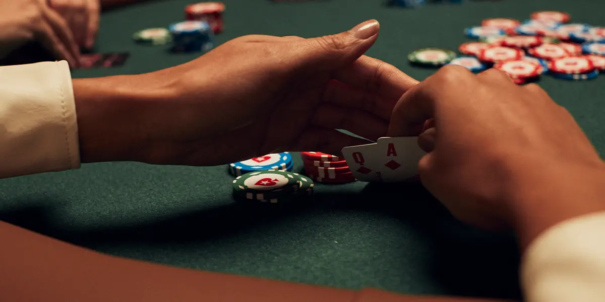 Jogador de poker segurando ás e dama do mesmo naipe, planejando sua próxima jogada estratégica.