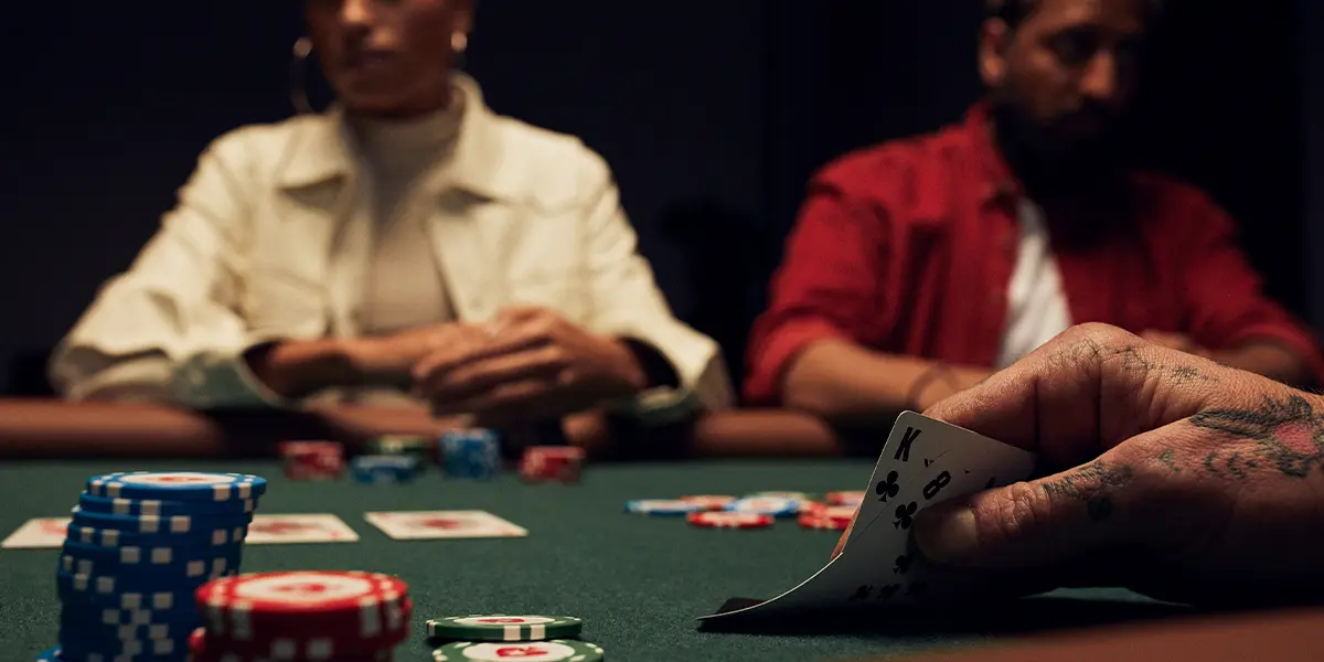 Close-up de um jogador de poker ao vivo segurando Rei e Oito de paus como cartas próprias, concentrando-se no processo de tomada de decisões com um par e uma pedida.